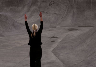 Rear view of woman in black standing against grey concrete 