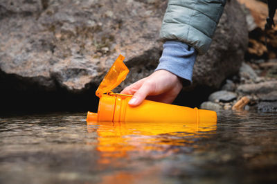 Close-up of female hands pouring drinking water from a mountain spring into a silicone bottle