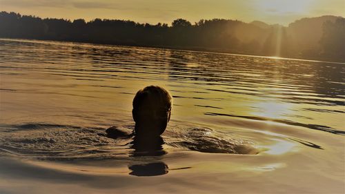 Silhouette woman swimming in lake during sunset