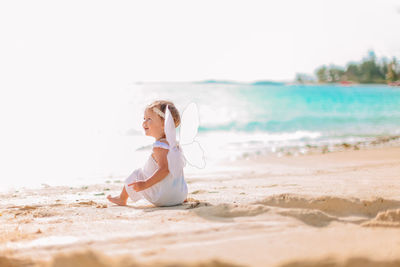 Full length of girl wearing costume sitting on beach against sky