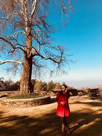 Full length of young woman standing on land against bare tree