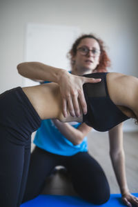 Crop anonymous fit woman in sportswear performing box pose with help of personal trainer during yoga session in studio