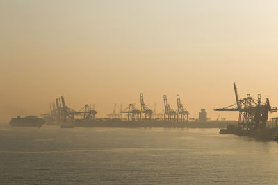 Cranes at commercial dock against sky during sunset