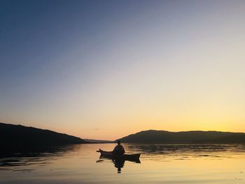 Silhouette person on lake against sky during sunset