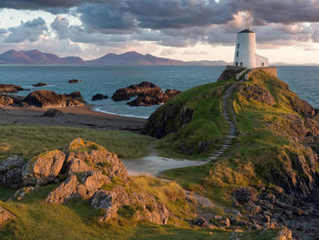 Lighthouse by sea against sky during sunset