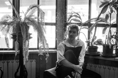 Portrait of young man  sitting near big old window with plants 