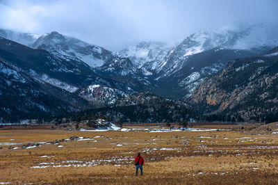 Rear view of woman walking on field against snowcapped mountains