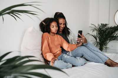 Happy mother and daughter taking selfie through smart phone at home