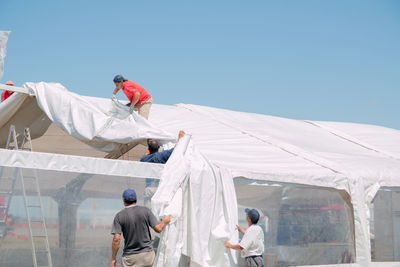 People covering greenhouse roof against clear sky