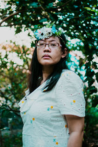 Portrait of young woman looking away against tree