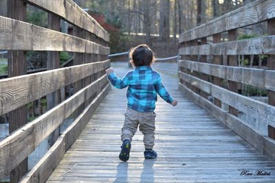 Rear view of boy walking on footbridge