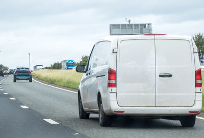 Vehicles on road against cloudy sky