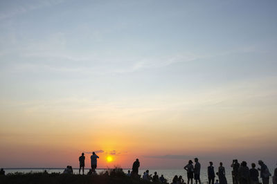 Silhouette people on beach against sky during sunset