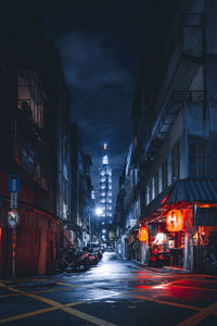 Illuminated street amidst buildings in city at night