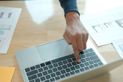 Cropped hand of businessman working at laptop on table in office