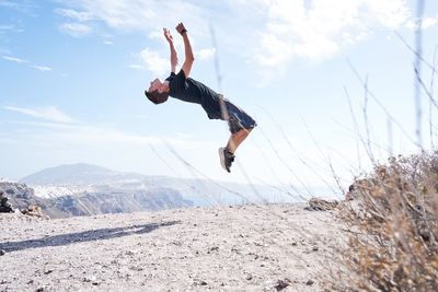 Full length of young man jumping against sky