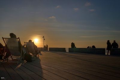 People by sea against sky during sunset