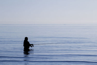 Silhouette man sitting on sea against sky