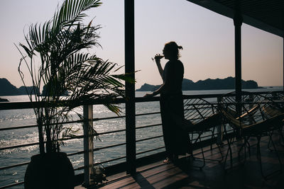 Silhouette woman standing by railing against sky during sunset