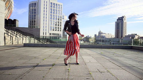 Full length of woman with umbrella against sky in city