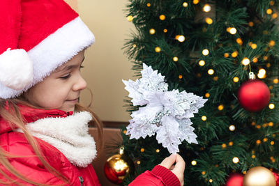 A girl in a santa hat admires looks at a christmas tree decoration. new year card.