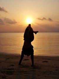 Silhouette man doing handstand at beach against sky during sunset