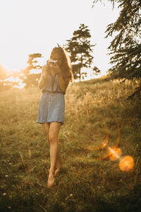 Young woman photographing while standing on grass against sky