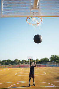 Front view of powerful energetic young african american sportsman playing basketball trying to hit the ball in net on playground