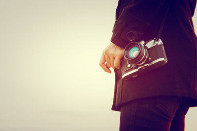 Midsection of woman standing with camera against sky