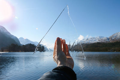 Cropped hand holding ice over river against clear blue sky