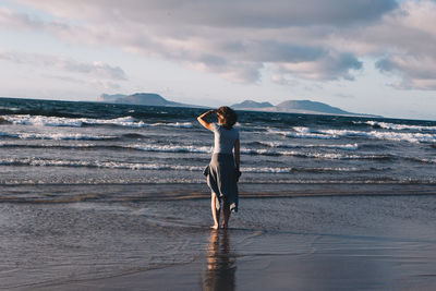 Rear view of woman standing at beach against sky