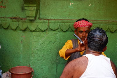 Rear view of man sitting against wall