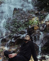 Side view of young man sitting on rock