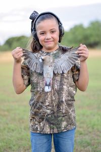 Portrait of smiling girl holding bird while standing on field