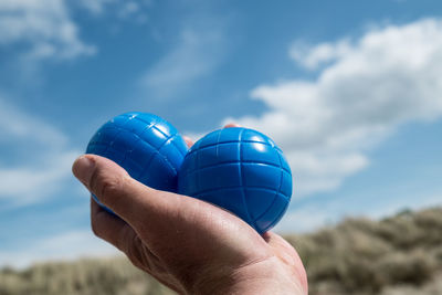 Cropped image of person holding blue balls against sky