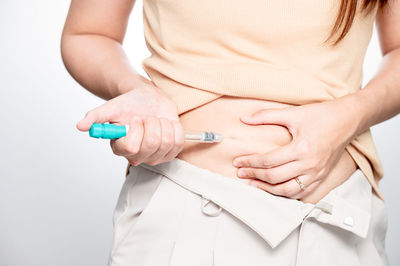 Midsection of woman holding syringe against white background