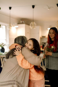 Cheerful girl embracing grandmother and greeting at home