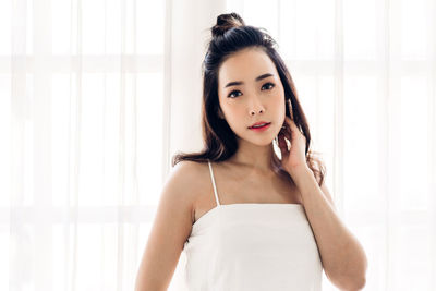 Portrait of beautiful young woman standing against window
