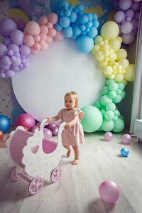 Baby girl in a pink dress is playing with a baby stroller toy