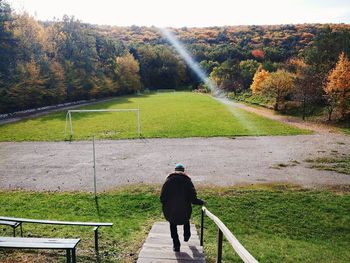 Rear view of man on steps against soccer field during autumn