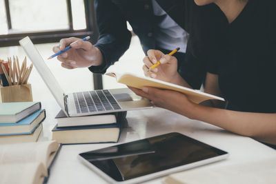 Cropped image of students using laptop while studying on table