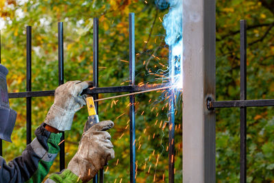 A welder using an electrode welds a metal fence in an autumn park, selective focus, copy space.