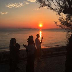 Silhouette people photographing sea during sunset