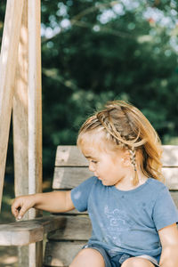 Girl looking away while sitting on wood