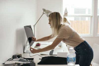 Side view of female graphic designer touching desktop monitor at home