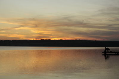 View of two men fishing at calm seaside at sunset