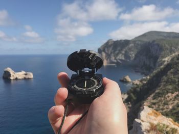 Close-up of hand holding navigational compass against sea