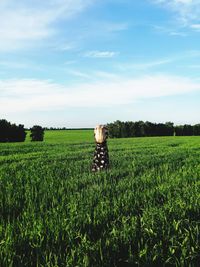 Rear view of woman standing by plants in agricultural field against sky