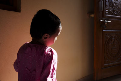 Boy looking away while standing against wall at home