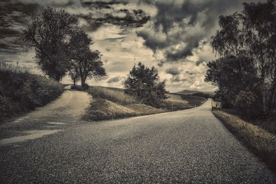 Road passing through landscape against cloudy sky